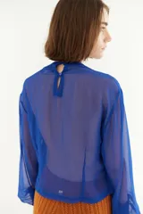 Blusa azul de crepe con transparencias y mangas largas abullonadas. Presenta detalle de lazos en los hombros y laterales.