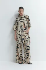 Vestido plisado color beige con estampado abstracto en negro, corte recto, cuello camisero y mangas cortas.