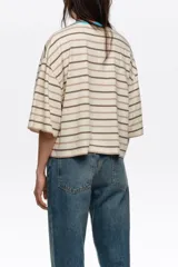 Remera boxy de algodón orgánico con diseño a rayas horizontales en negro y crudo, escote redondo con ribete amarillo, mangas cortas amplias y pequeño bordado en el pecho.