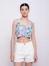 Top blanco con estampado floral en tonos naranja y lila, de corte cropped y breteles anchos.