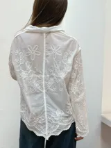 Camisa de encaje color crema con diseño floral bordado, cuello camisero, cierre frontal de botones y mangas largas con terminación acampanada.