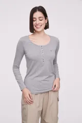 Remera blanca de manga larga, entallada, con cuello redondo y una hilera de botones en el frente. Incluye un pequeño bolsillo decorativo en el pecho.