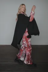 Ruana de tejido de punto color negro, con diseño abierto, flecos en el ruedo y bolsillos frontales destacados con bordados artesanales en tonos contrastantes.