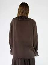 Blusa de manga larga color marrón, con cierre frontal de botones, escote en V y detalles de volados fruncidos alrededor del cuello y los puños elásticos.