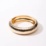 Brazalete rígido dorado con textura acanalada y cierre a presión.