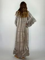 Vestido largo de corte holgado con estampado tie-dye en tonos grisáceos. Presenta escote redondo con cordones ajustables y borlas, mangas tres cuartos con volados y ruedo con volado amplio.