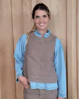 Chaleco de denim color marrón con pespuntes en contraste, cuello redondo y diseño de corte recto. Presenta un estilo versátil ideal para superponer sobre camisas o usar como prenda única.