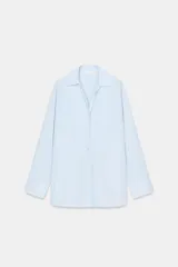 Camisa de popelín confeccionada en algodón, con cuello solapa, escote en pico y cierre frontal con botones. Presenta mangas largas con puños y un bajo redondeado asimétrico.