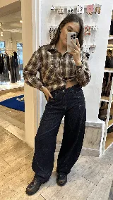 Camisa de corte relajado confeccionada en algodón con estampado de cuadros tartán en tonos marrones y beige. Presenta cuello clásico, cierre frontal de botones, mangas largas con puños abotonados y un bolsillo frontal en el pecho.