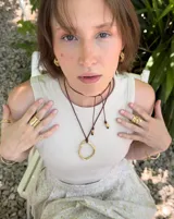 Collar con dije colgante de forma orgánica e irregular, acabado dorado, suspendido de un cordón negro de algodón natural.