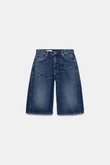 Bermuda tipo jorts de denim con efecto lavado, tiro medio y corte holgado. Presenta diseño de cinco bolsillos, trabillas para cinturón, costuras laterales torcidas y cierre frontal con cremallera y botón metálico.