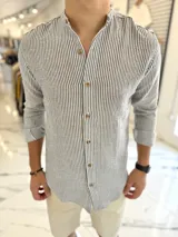 Camisa de lino a rayas verticales grises y blancas, con cuello mao y cierre frontal de botones marrones.