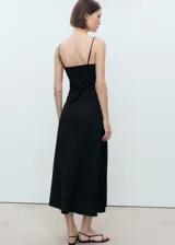 Vestido midi negro con tirantes finos, escote en V y detalle de lazo en el centro del busto. Diseño recto sin mangas y sin cierre.