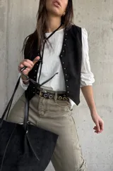Chaleco negro de gamuza con detalles de tachas doradas a lo largo de la abertura frontal y los bordes.
