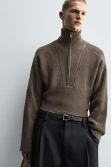 Jersey de punto de corte relajado, color marrón, con cuello perkins y cierre frontal de cremallera. Presenta manga larga y acabados en rib en puños y bajo.