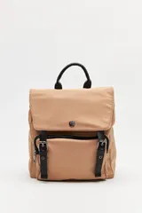 Mochila urbana de nylon color beige, con solapa superior, bolsillo frontal con cierre y correas decorativas con hebillas metálicas. Incluye manija superior y correas ajustables.