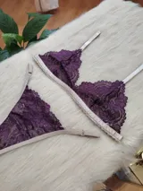 Conjunto de lencería compuesto por un bralette triangular y una bombacha tipo tanga, confeccionados en encaje color violeta con terminaciones y breteles en color tostado.