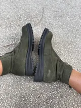 Botas cortas de gamuza en color verde oliva, con suela track negra de goma y cierre frontal. Presentan un diseño minimalista y versátil.