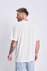 Remera de corte oversize color crudo, con cuello redondo, mangas cortas y estampa frontal con la frase 'Good Wave' en letras azules.