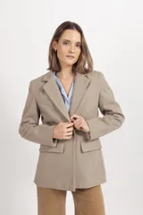 Blazer de paño fantasía en color beige, con solapas clásicas, cierre frontal de botones y dos bolsillos delanteros con solapa. Presenta una estructura entallada con forro interior.