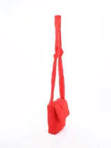 Mochila pequeña acolchada color rojo con patrón de rombos. Tiene solapa con cierre magnético y correa de hombro acolchada.