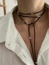 Corbatín tipo choker de tiento de gamuza marrón, con diseño de doble vuelta y cuentas metálicas plateadas distribuidas a lo largo de las tiras.