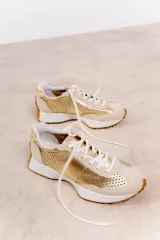 Zapatillas deportivas color blanco con detalles en beige y suela marrón.