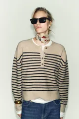Jersey de punto de manga larga con cuello redondo y cierre frontal parcial con botones. Presenta un diseño a rayas horizontales en contraste sobre fondo beige.