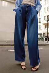 Jeans de tiro alto con corte loose fit y pernera holgada. Presenta detalle de corchetes en la cintura, bolsillos frontales y bolsillos de plastrón en la parte trasera. Cierre frontal con cremallera y botón.