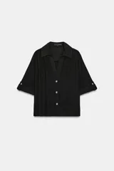 Camisa negra de textura arrugada, con cuello solapa, escote en V y cierre frontal de botones. Cuenta con mangas cortas terminadas en vuelta con trabilla y botón.