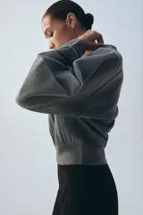 Chaqueta estilo bomber de punto color beige con acabado brillante, cuello redondo, manga larga con puños elásticos y cierre frontal con cremallera.
