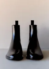 Botín tipo Chelsea de cuero vacuno color negro, con paneles laterales elásticos y tirador trasero. Presenta una silueta clásica con punta redondeada y suela plana de resina de poliuretano.