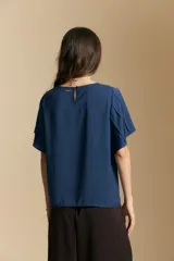 Top de color azul, con escote redondo a la base y mangas cortas amplias con caída fluida. Presenta una silueta relajada y un diseño minimalista.