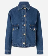 Campera de jean azul de corte recto y holgado, con cuello camisero, cierre frontal de botones metálicos dorados, bolsillos frontales con solapa y mangas largas con puños abotonados.