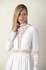 Vestido midi blanco con detalles de encaje color beige en cuello, mangas, cintura y ruedo. Tiene cuello alto con lazo y mangas largas.