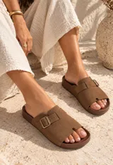 Sandalias planas de color beige con diseño de tira ancha en el empeine, hebilla metálica ajustable lateral y plantilla anatómica.