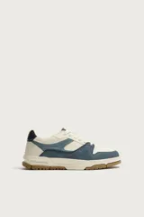 Zapatilla de básquet con cordones, diseño urbano de caña baja. Parte superior confeccionada en combinación de cuero sintético blanco y piezas de denim azul, con suela chunky de goma marrón y entresuela blanca.