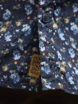 Camisa de hombre azul marino con estampado floral en tonos celeste y amarillo, de manga larga y corte clásico.