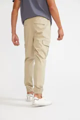 Pantalón cargo color beige con ajuste slim, cintura elástica con cordón ajustable, bolsillos laterales con solapa y velcro, y puños elásticos en los tobillos.