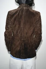 Blazer de ante color marrón, con cuello solapa, hombreras, manga larga y cierre frontal cruzado con botones. Cuenta con bolsillos delanteros de doble vivo.