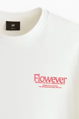 Remera de algodón blanca de corte holgado, con cuello redondo y diseño estampado en el pecho con texto en color rojo.