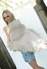 Poncho de tejido de algodón color beige claro, con diseño de punto calado y flecos en el borde inferior.
