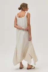 Vestido largo color crema, con breteles anchos y escote recto. Presenta corte irregular en el ruedo y volado en el bajo.