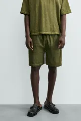 Bermuda de algodón color verde oliva, con corte relajado y textura acanalada vertical. Presenta cintura elástica con cordón interior y bolsillos laterales y trasero.