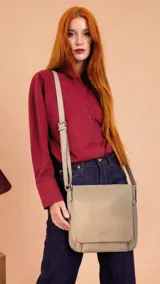 Bandolera de diseño minimalista con tapa frontal, confeccionada en material símil cuero color beige. Cuenta con correa larga ajustable, compartimento principal con cierre y divisiones internas para mayor organización.