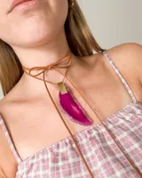 Gargantilla con tiento de cuero marrón que se ata al cuello y dije de piedra ágata fucsia con borde gris y aplique dorado.