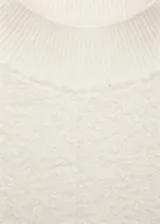 Buzo de tejido bouclé color crudo, con cuello perkins, manga larga y diseño recto con terminaciones de canalé.