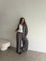 Conjunto de camisa y pantalón de viyela a cuadros en tonos marrón, blanco y azul. La camisa es oversize de manga larga con bolsillos frontales y cierre de botones. El pantalón es recto y holgado.