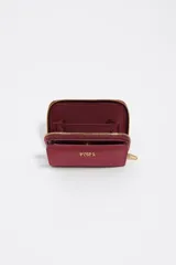 Billetera compacta de nylon color beige, con cierre de cremallera perimetral y tirador decorativo con cordón. Presenta el logo metálico de la marca en el frente.