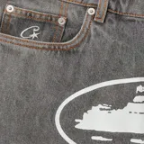 Short de jean gris con estampado blanco ovalado en el frente. Corte holgado y largo a la rodilla. Marca Corteiz, modelo Alcatraz.